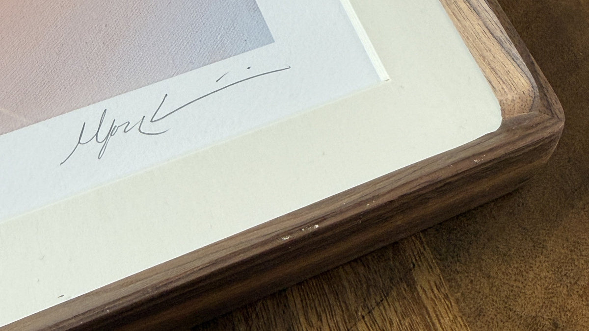 Corner of the Nuqta artist proof in a solid walnut frame with a cream mat, the pencil signature visible on the paper