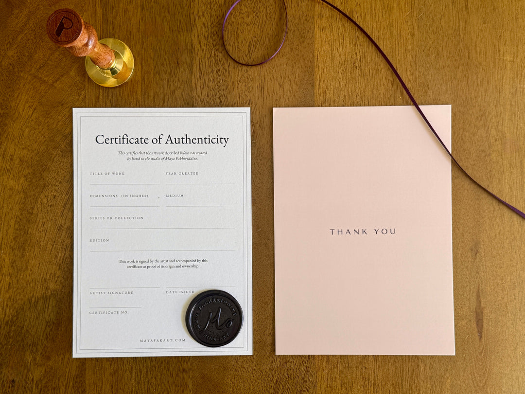 The certificate of authenticity and a thank you card laid on a wood table, included with every Noon print