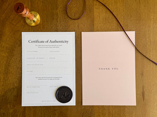 The certificate of authenticity and a thank you card laid on a wood table, included with every Nuqta print